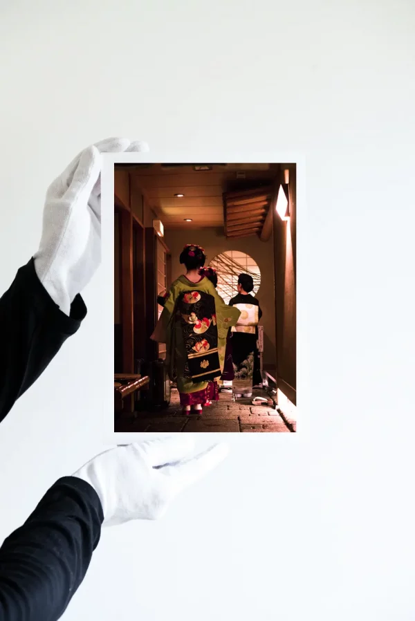 Deux mains dans des gants blancs tiennent une impression de trois geisha en kimonos richement brodés attendent dans le hall d’un salon de thé à Gion Kyoto.