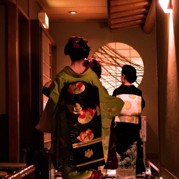 Trois geisha japonaises vêtues de kimonos traditionnels richement brodés attendent dans le hall d’un salon de thé à Gion Kyoto.