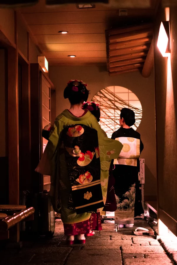 Trois geisha japonaises vêtues de kimonos traditionnels richement brodés attendent dans le hall d’un salon de thé à Gion Kyoto.
