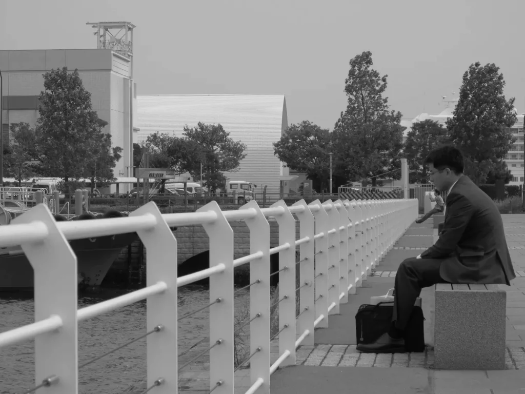 Jeune salaryman japonais en costume assis sur un banc en face de la baie de Yokohama à Tokyo, perdu dans ses pensées.