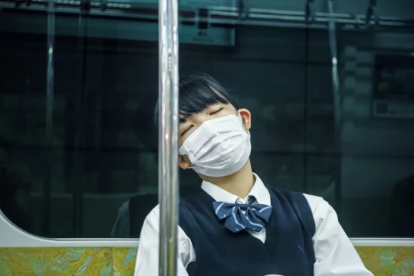 Une jeune fille japonaise dans son uniforme de lycéene qui porte un masque dort dans le métro.