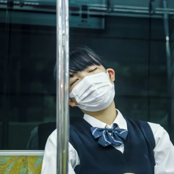 Une jeune fille japonaise dans son uniforme de lycéene qui porte un masque dort dans le métro.
