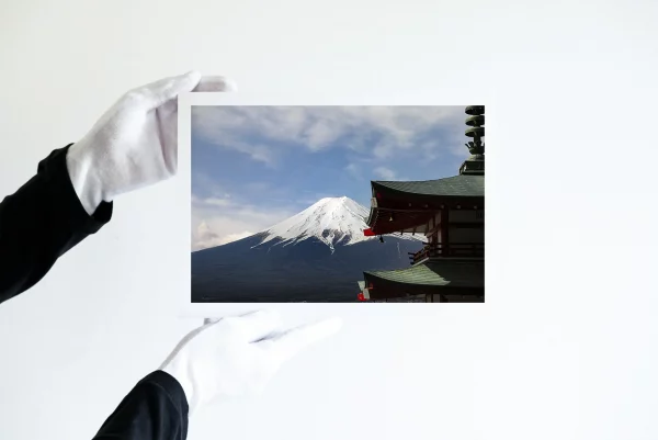 Deux mains dans des gants blancs tiennent une impression d'une vue du Mont Fuji enneigé en arrière plan depuis la pagode de Chureito dans la ville de Fujiyoshida.