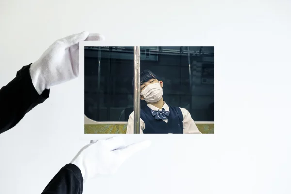 Deux mains dans des gants blancs tiennent une impression d'une jeune fille japonaise dans son uniforme de lycéenne qui porte un masque dort dans le métro.