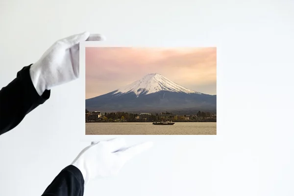 Deux mains dans des gants blancs tiennent une impression d'un vieux bateau sur le lac Kawaguchi devant le Mont Fuji le ciel embrasé par le couché de soleil