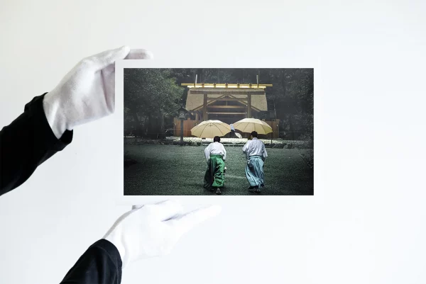 Deux mains dans des gants blancs tiennent une impression de deux prêtres shinto tenant des parapluies jaunes dans la forêt embrumée d'Ise Jingu