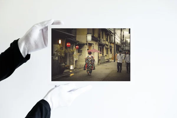 Deux mains dans des gants blancs tiennent une impression d'une geisha tenant un parapluie rouge descend une rue de Kyoto